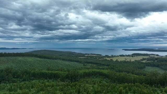 southern tasmania coastline, looking at bruny island with storm clouds and rain over the ocean, flying above a beach town and cattle, cow farm, in australia