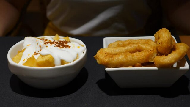 Patatas bravas and rabas (deep fried battered calamares), typical tapas food at Spain. Closeup shot of two small bowls. Papas cubes topped with mayo, large tasty rings of squid near