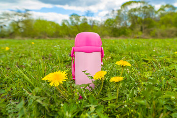 Children's pink thermos on green grass. Rreusable thermo bottle for drinks, water, tea. Flask for resting and relax outdoors