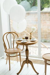 Table setting for a third birthday tea party at the cafe on a sunny day. Panoramic windows, white air balloons