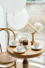 Table setting for a third birthday tea party at the cafe on a sunny day. Panoramic windows, white air balloons