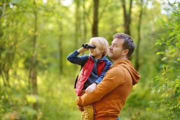 Schoolchild and his father hiking together and exploring nature. Child looking through a binoculars. Little boy with dad spend quality family time in sunny summer forest. Fatherhood