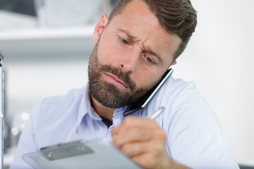 Fototapeta premium businessman writing on clipboard while holding mobile