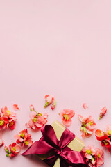 Happy Mothers day. Stylish gift box with red flowers on pink background flat lay. Greeting card template with space for text. Festive craft gift with ribbon and flowers border. Women's day