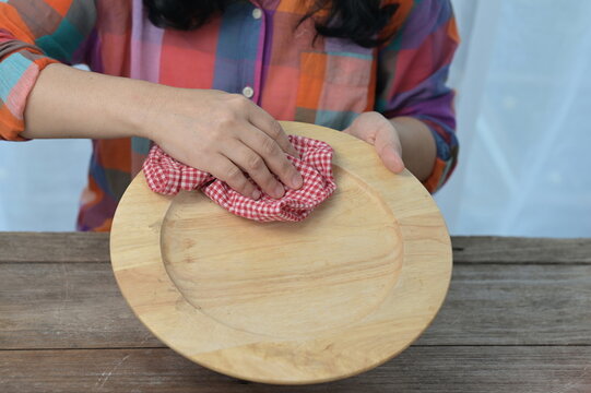 A housewife in brightly colored check  clothes is dry the dishes. The woman's right hand holds a red (plaid) dishcloth, wipes a large plate made of wood before placing it in a dish rack. 
