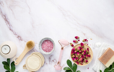flat lay with organic sea salt with dried rose flowers, soap, candle, brush and gua sha on a pink marble background. The concept of a natural spa product. Top view and copy space