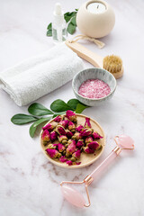 Organic sea salt for the body with dried rose flowers, candle, brush, towel and gua sha on a pink marble background. The concept of a natural spa product. Skin care
