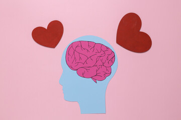 Paper-cut head with brain and hearts on pink background. Falling in love concept