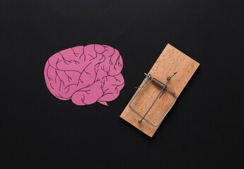 Paper cut brain with a mousetrap on black background. Fake information, brain tricks