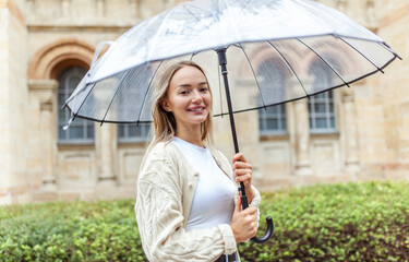 Portrait of a cute smiling woman with a transparent umbrella in the city. Lifestyle