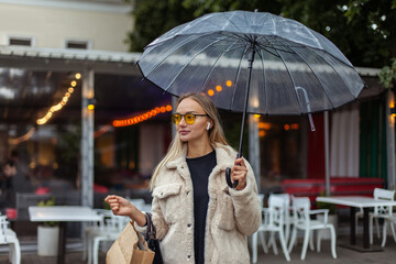 Portrait of a young fashion woman with an umbrella and a shopping bag spends time in the evening city