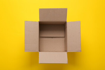 Open empty cardboard box on yellow background. Top view