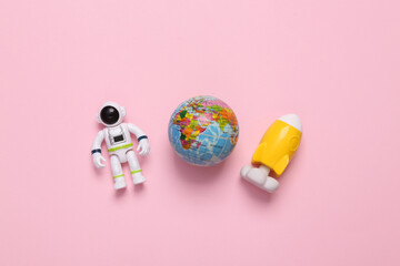 Astronaut toy model with space shuttle and globe on pink background. Space mission. Flat lay