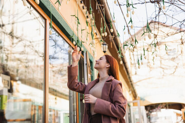 cheerful redhead woman in coat smiling while looking at hanging tulips outside.