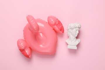Pop concept. David bust with an inflatable flamingo on a pink background. Top view