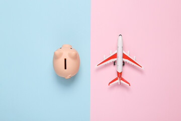 Travel concept. Toy model of passenger plane with piggy bank on blue pink pastel background. Top...
