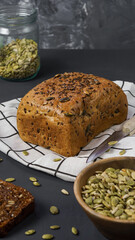 cereal bread with sunflower and pumpkin seeds, bread wrapped in a kitchen towel on a dark background