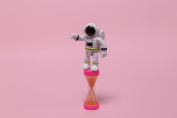 Space mission concept or startup. Astronaut in a spacesuit figurine with hourglass on pink...