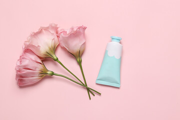 Cream bottle with flowers isolated on pink background. Beauty still life. Flat lay