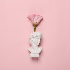 Romantic minimal still life. David bust with flower isolated on pink background