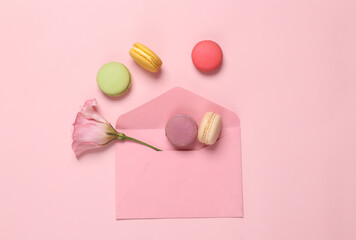 Romantic still life, envelope with macarons and a flower on a pink background. Creative layout. Flat lay