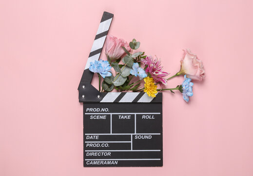 Romantic concept. Movie clapperboard with flowers on a pink background. Creative layout. Flat lay