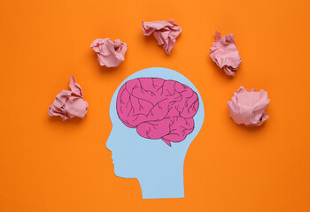 Paper-cut head and crumpled ball of paper on orange background. Lack of ideas