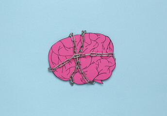 Paper brain wrapped with a steel chain on a blue background. Lack of ideas or headache