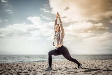 Attractive fit woman practicing yoga asana on the beach at bright sunny day. Warrior 1 pose.
