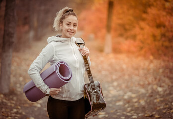 Attractive sporty woman with bag and mat goes to workout in autumn forest or park