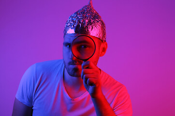 Bearded Man in Foil Hat Holds Magnifier in Red Blue Neon Light