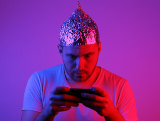 Crazy Bearded Man in Foil Hat Plays with Smartphone in Red Blue Neon Light.