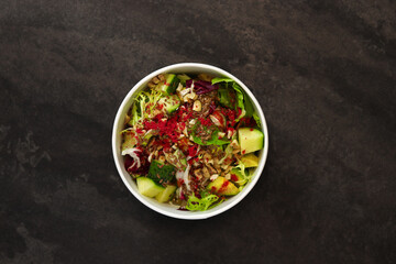 Vegetarian salad with cucumbers, lettuce, walnuts and flax seeds in a round takeaway paper container on dark background. Healthy food, restaurant dish delivery. Top view. Free space for text