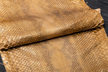 golden brown metallic dyed folded natural genuine python leather on the wooden table	