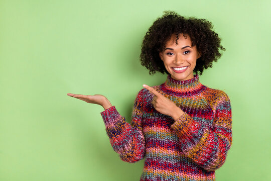 Photo of optimistic young valume hairdo lady hold index empty space wear colorful pullover isolated on green color background