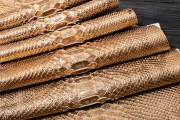 golden brown metallic dyed folded natural genuine python leather on the wooden table	