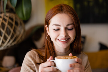 young cheerful woman smiling and holding cup of latte in cafe.