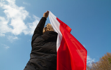 Woman holding flag of Poland against blue sky. 3 May Polish Constitution Day (3rd May National Holiday) or Independence Day celebration.