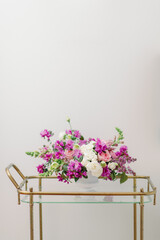 purple pink and white flower centerpiece in white vase on bar cart
