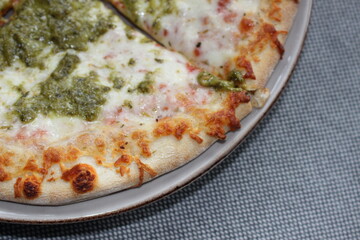 Pizza Magherita with green pesto on it and a nice crispy and brown baked edge and cheese on it on plate wich is being on a fabric material