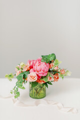 pink and peach flowers and ivy in glass vase against neutral wall