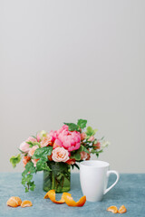 Obraz na płótnie Canvas pink and peach flower centerpiece with white coffee mug and clementine