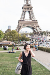 Female tourist in black jumpsuit smiling in front of Eiffel Tower