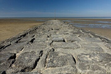 Basalt groin (groyne) at sandy North Sea beach at low tide under a blue spring sky (horizontal),...