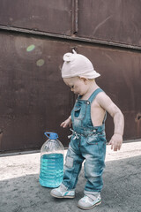 one-year-old child in overalls looks at bottle of antifreeze