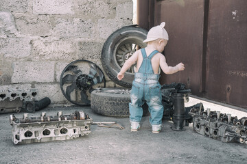 one year old baby playing mechanic among auto parts, standing with his back