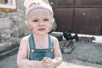one-year-old baby in overalls with dirty sad face stands and looks at camera