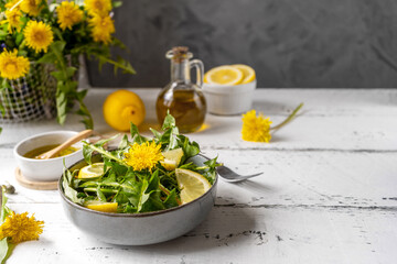 Dandelion salad with olive oil, lemon juice and spices on white wooden table with grey background. Copy space - obrazy, fototapety, plakaty
