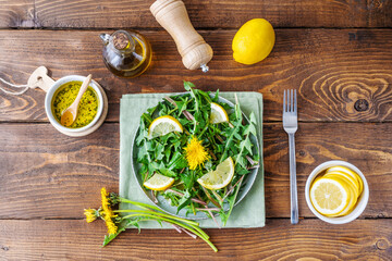 Dandelion salad with dip made with olive oil, lemon juice and spices on brown wooden table. Top view