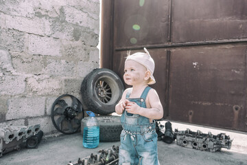 one year old baby plays among car parts and looks forward up in thought